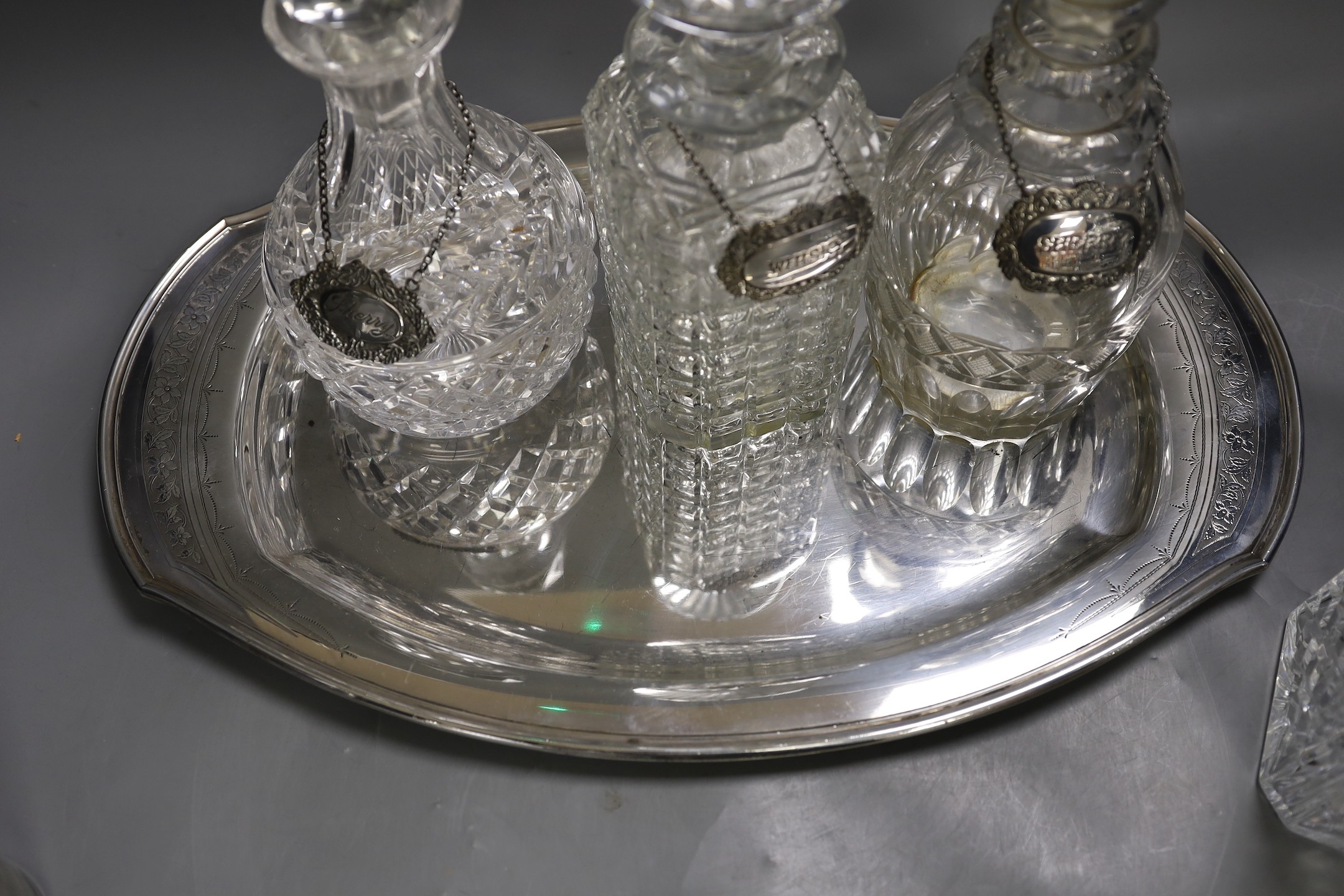 A silver plated oval tray, five assorted cut glass decanters and five assorted silver wine labels.